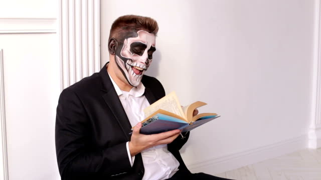 Un-hombre-con-un-maquillaje-terrible-en-forma-de-un-cráneo-sostiene-un-libro-en-sus-manos.