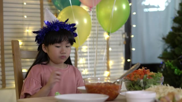 Asiatische-Kindermädchen-warten-Vater-und-Mutter-kommen-nach-Hause-Geburtstagsfeier-und-Abendessen-zusammen.-Unglückliche-Familienzeit-zu-Hause.-Konzept-von-einsam,-enttäuscht-und-traurig.