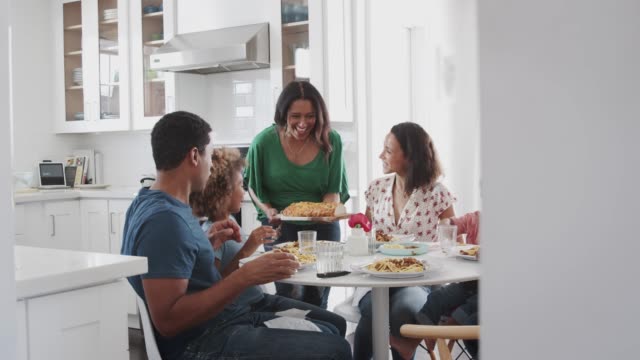 Großmutter-mittleren-Alters,-die-gemischte-Rasse-Mehrgenerationenfamilie-serviert,-die-gemeinsam-in-der-Küche-isst