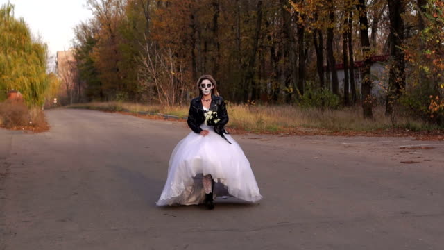 Mädchen-in-Hochzeitskleid-mit-einer-Totenkopfmaske-auf-ihrem-Gesicht-läuft-auf-einer-leeren-Straße