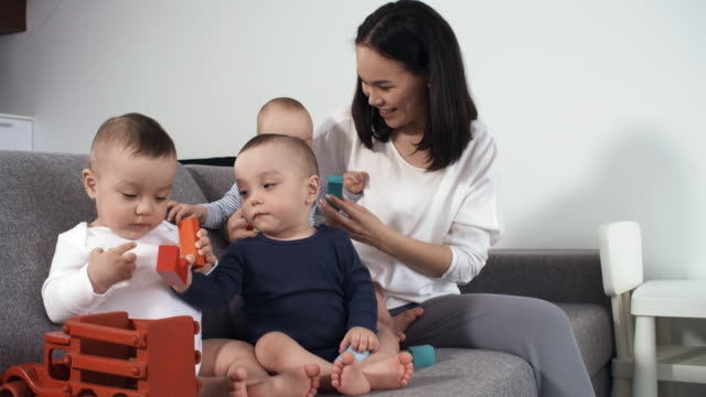 1-Jahre-alte-Mixed-Race-Triplets-sitzen-auf-Couch-mit-Mama
