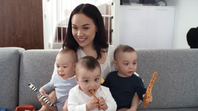 Mixed-Race-Mutter-posiert-mit-ihren-Triplets-auf-Couch