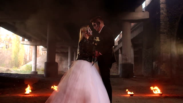 Couple-in-bridal-gowns-with-halloween-makeup-with-fire-burning-around-them.