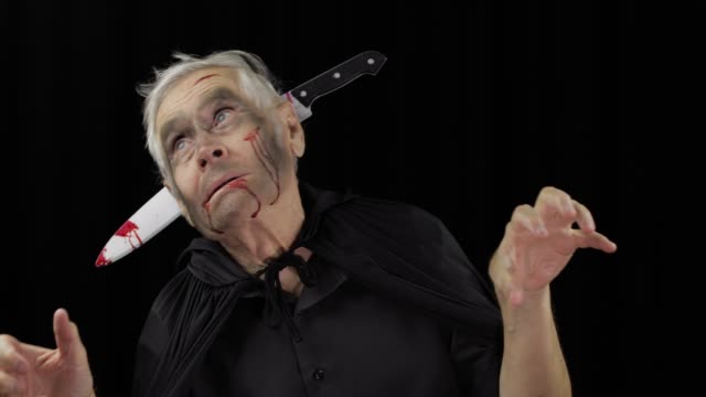 Elderly-man-with-knife-in-head.-Halloween-makeup-and-costume.-Blood-on-his-face