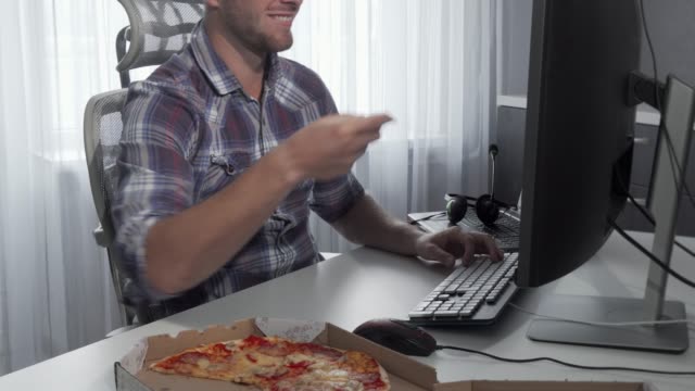 Schöne-Mann-genießen-leckere-Pizza-während-der-Arbeit-am-Computer