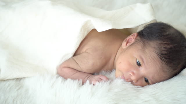 4K-Medium-shot-of-relaxing-sleepy-little-asian-newborn-baby-boy-son-lying-down-on-white-bed-with-blanket-in-home-bedroom.-Cute-innocent-newborn-baby-health-care-and-sensitive-skin-concept.