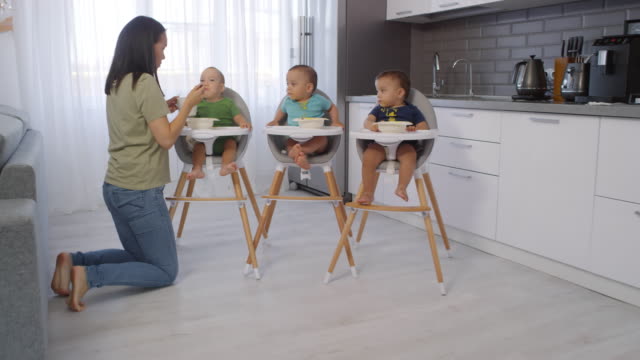 Asiática-mamá-alimentando-el-puré-a-los-trillizos-del-niño-pequeño