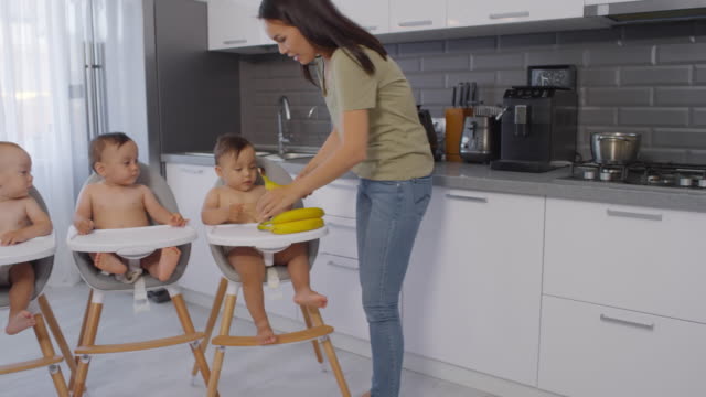 Asiática-mamá-dando-plátanos-a-los-trillizos-del-niño-pequeño