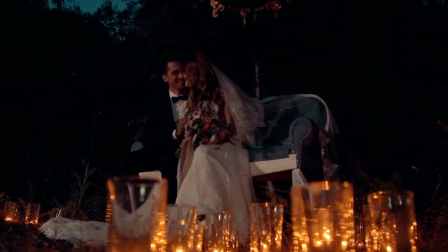 The-newlyweds-embrace-and-kiss-at-night,-sitting-on--couch-in-a-dark-forest.