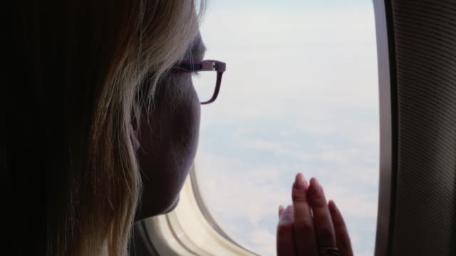 Eine-Frau-in-Gläsern-befasst-sich-mit-dem-Flugzeugfenster.-Silhouette,-Rückansicht