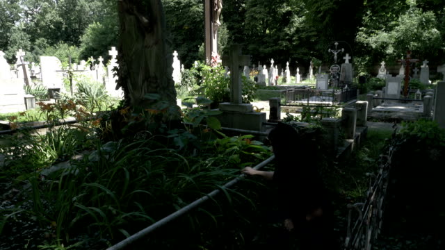 Begräbnis-Frau-Witwe-platzieren-eine-Krone-auf-alten-Grab-mit-Statue-bedeckt-mit-Moos-Efeu-und-Unkraut-Weinen-Sie-ihr-Knie-schmerzte