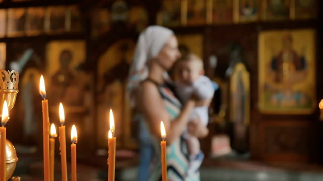 Burning-candles-in-church,-mother-with-baby-on-blurred-background
