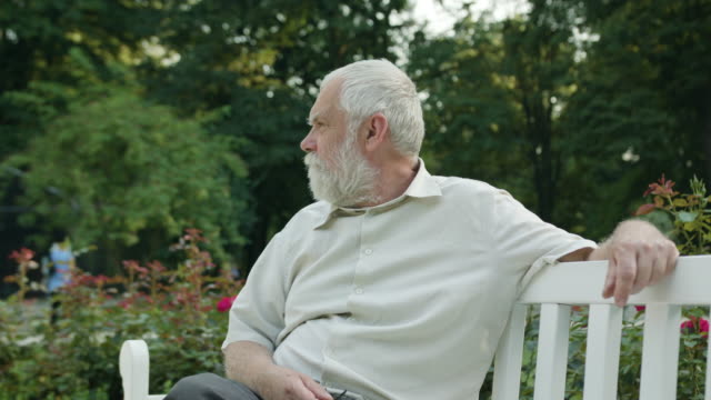 Alter-Mann-sitzt-auf-einer-weißen-Bank-im-Park