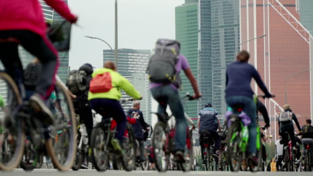 Bike-city-events-competition-in-background-of-skyscrapers,-crowd-of-cyclists-from-thousands-of-people-riding-bicycles,-unrecognizable-people-in-blur