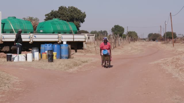 One-old-african-woman-collecting-water-from-a--tanker-and-pushing-it-in-a-wheelbarrow-back-to-her-home