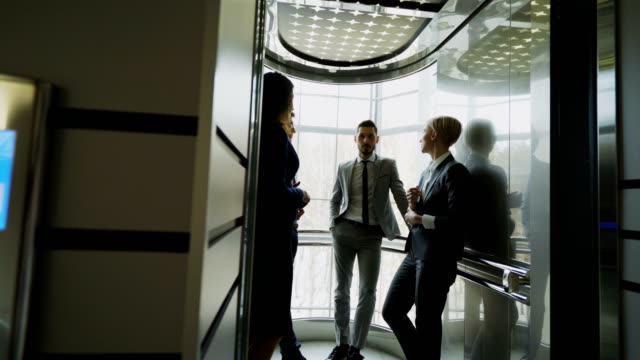 Tracking-Schuss-von-Unternehmerinnen-und-Unternehmern-Kollegen-reden-im-Aufzug-und-darauf-vorbereiten,-in-modernen-Business-Center-nach-unten-verschieben