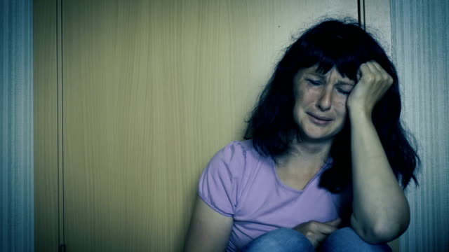Violence-in-family.-Young-woman-is-crying-while-sitting-on-floor-in-corner-of-room.-Close-Up-Of-A-Scared-And-Crying-Woman-With-Smeared-Make-Up.-Girl-crying-in-corner-and-feeling-lonely.
