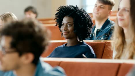 Klug-und-schön-junge-schwarze-Mädchen-hört-einen-Vortrag-in-einem-Klassenzimmer-voller-Multi-ethnischen-Studenten.-Geringe-Schärfentiefe.