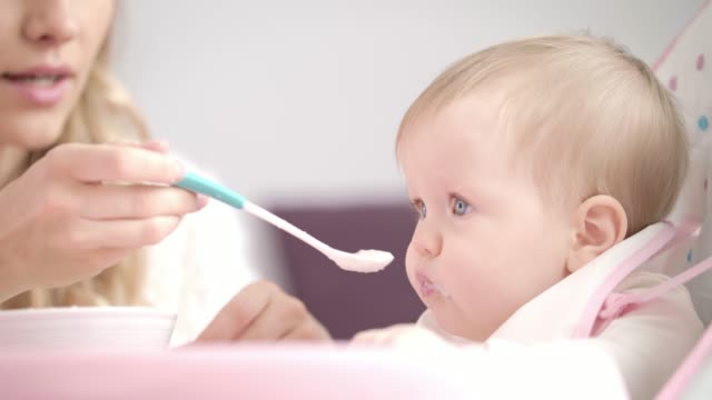 Baby-eating-puree-with-spoon.-Mother-feeding-child-with-porridge