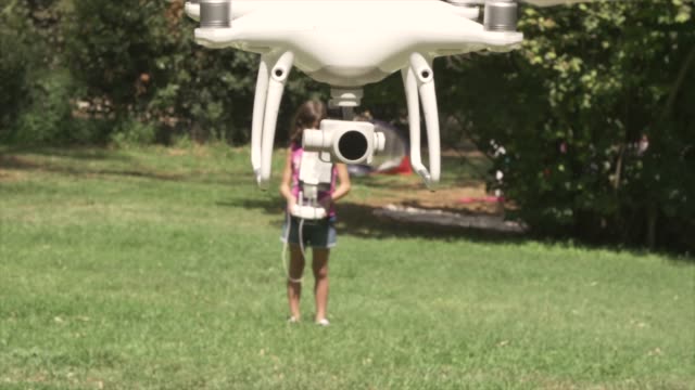 Young-little-girl-flying-a-drone-playing-outdoor-on-summer-in-green-grass-field-remote-pilot-slow-motion