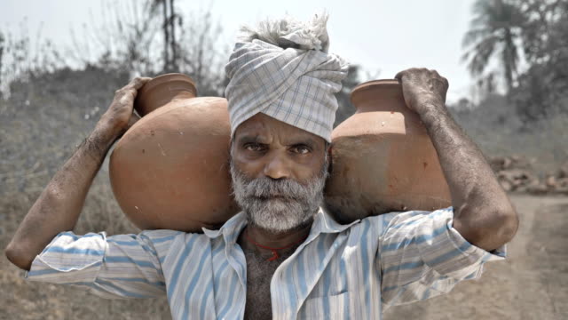 Tired-poor-man-carrying-clay-pots-and-standing-in-barren-farmland-under-the-hard-sun