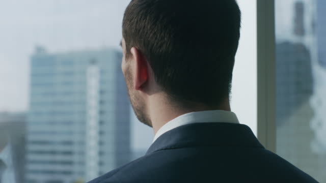 Close-up-Shot-of-the-Thoughtful-Businessman-in-a-Suit-Standing-in-His-Office-and-Contemplating-Next-Big-Business-Deal,-Looking-out-of-the-Window.-Big-City-Business-District-Panoramic-Window-View.