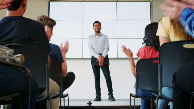 Estudiantes-aplauden-profesor-presentación-delante-de-pantalla