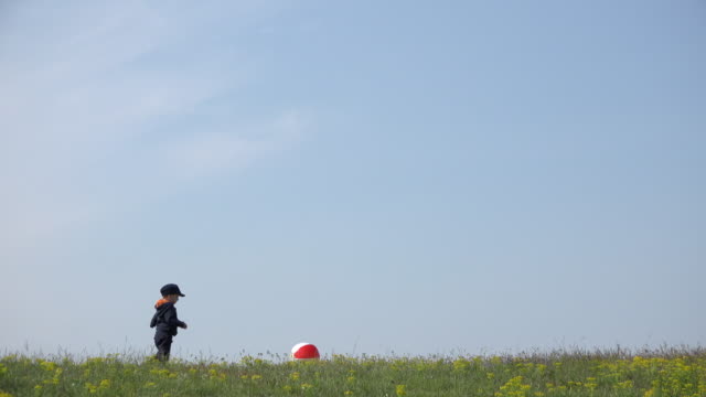 Niño-pequeño-jugando-con-bola-grande-en-la-cresta-de-la-colina,-sereno-cielo-4K