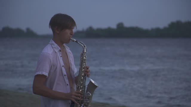 Handsome-young-guy-is-playing-the-saxophone-on-the-river-bank