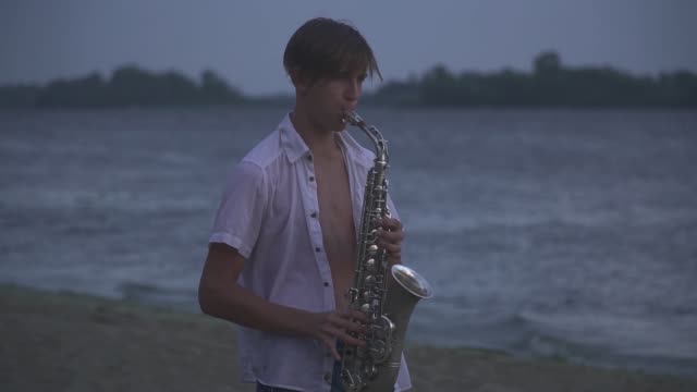 Chico-joven-guapo-es-jugar-el-saxophone-en-la-orilla-del-río