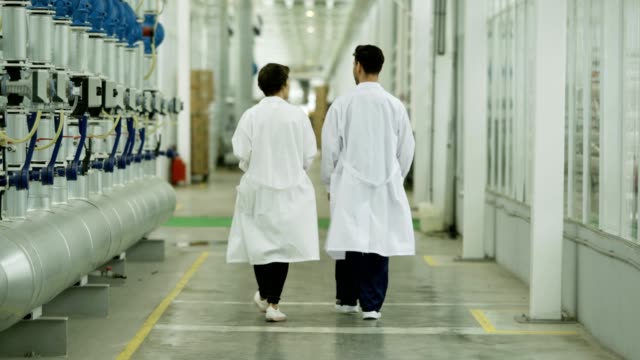 Rear-view-of-two-scientists,-man-and-woman,-walking-along-corridor-in-modern-agricultural-complex-and-talking,-follow-shot