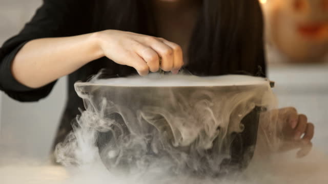 Witch-conjuring,-putting-magic-spell-and-cooking-potion-in-pot-with-white-smoke