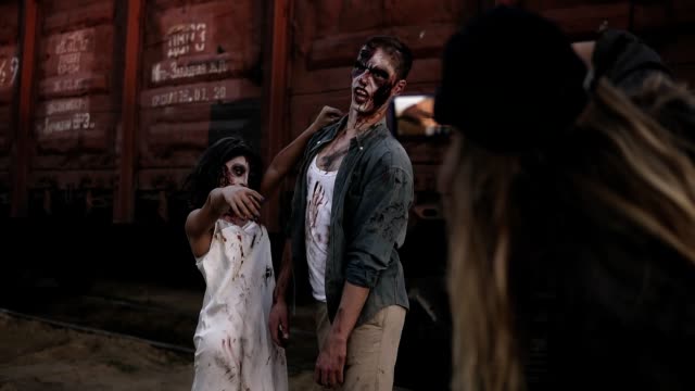 The-girl-from-the-backstage-making-a-photo-with-her-mobile-of-two-zombies-standing-in-front-the-wagon-outdoors.-Horror,-halloween,-staging-concept