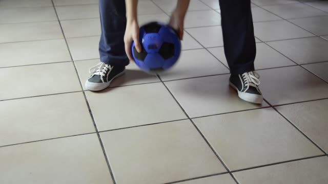 Detalle-de-pie-de-niño-jugando-con-balón-en-el-suelo-en-casa