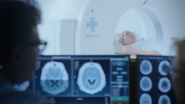 In-Medical-Laboratory-Patient-Undergoes-MRI-or-CT-Scan-Process-under-Supervision-of-Radiologist-in-Control-Room,-He-Watches-Procedure-and-Monitors-Brain-Activity-Results.