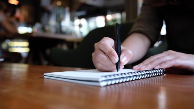 Lenta-de-la-mano-de-una-mujer-escribiendo-en-cuadernos-en-blanco-de-madera-mesa-de-café