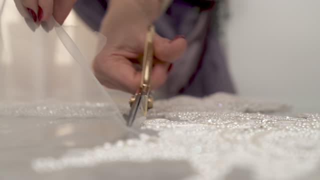 A-closeup-of-woman's-hands-cutting-out-sequined-and-beaded-lace-following-its-shape-and-putting-the-scissors-on-the-table-in-the-end