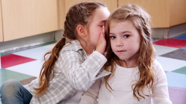 Two-elementary-schoolgirls-whispering-in-class