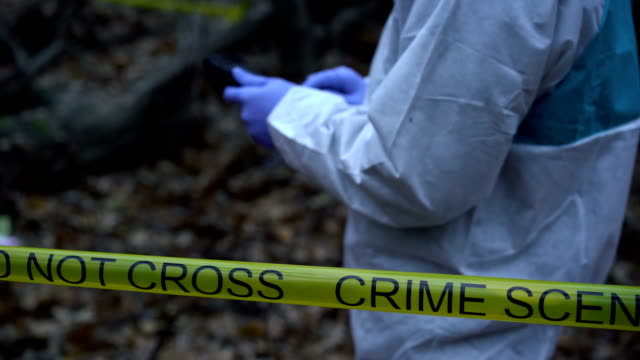 Crime-scene-expert-entering-data-on-tablet-at-murder-site,-collecting-evidence