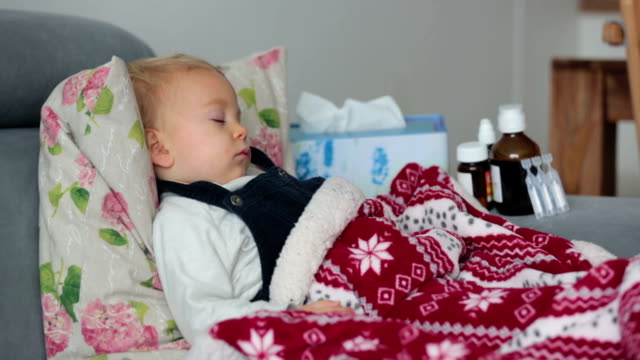 Niño-enfermo,-durmiendo-cubierto-con-una-manta-suave-en-el-sofá-en-la-sala-de-estar,-junto-a-él-la-medicina
