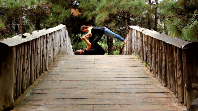 Man-and-woman-praticing-acro-yoga-on-top-of-bridge-in-park