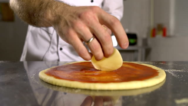 Hand-Chef-legt-Käse-in-Pizza-basieren-auf-Tomaten-Soße-Nahaufnahme