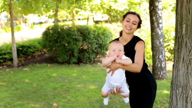 Una-joven-madre-feliz-camina-con-su-hijo-recién-nacido-en-el-parque-en-verano.
