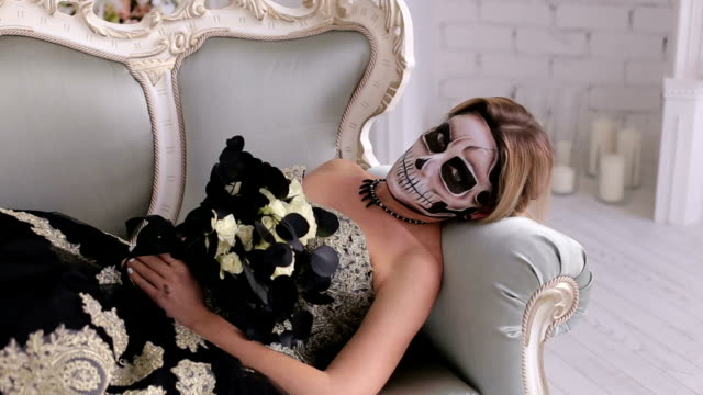 Creepy-woman-in-dress-and-with-makeup-in-the-form-of-a-skull-lies-on-retro-sofa
