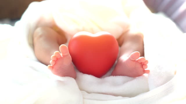 Baby-newborn-moving-foot-and-red-heart-in-beautiful-light-on-white-background