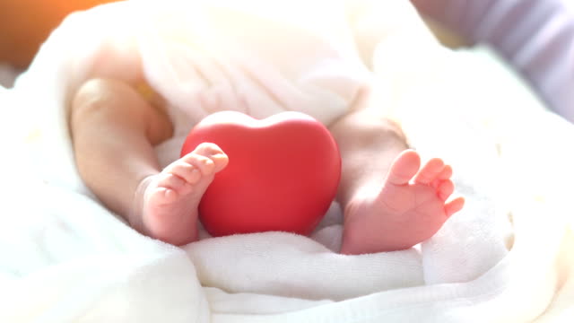 Baby-newborn-moving-foot-and-red-heart-in-beautiful-light-on-white-background