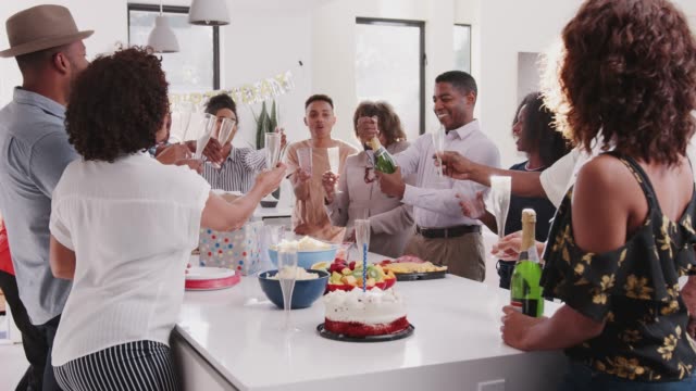 Hombre-negro-de-mediana-edad-abriendo-champán-y-sirviendo-durante-una-celebración-en-casa-con-su-familia