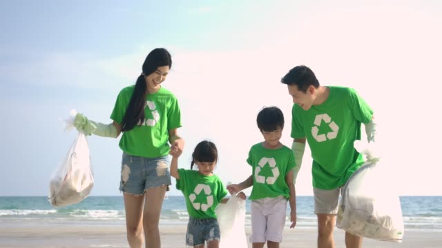 Grupo-de-voluntarios-en-camisetas-verdes-limpiando-la-playa-con-bolsas-de-plástico-llenas-de-basura.-Cámara-lenta.-Concepto-ecológico-seguro.-resolución-4k.