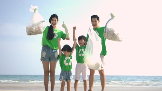 Group-of-volunteers-in-green-t-shirts-cleaning-up-the-beach-with-plastic-bags-full-of-garbage.-Slow-Motion.-Safe-ecology-concept.-4k-resolution.