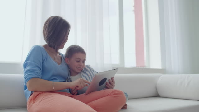 Mutter-und-Sohn-spielen-mit-digitalen-Tablet-zu-Hause.-Junge-Mutter-mit-ihrem-5-Jahre-alt-lächelnd-mit-digitalen-Tablet-zu-Hause.